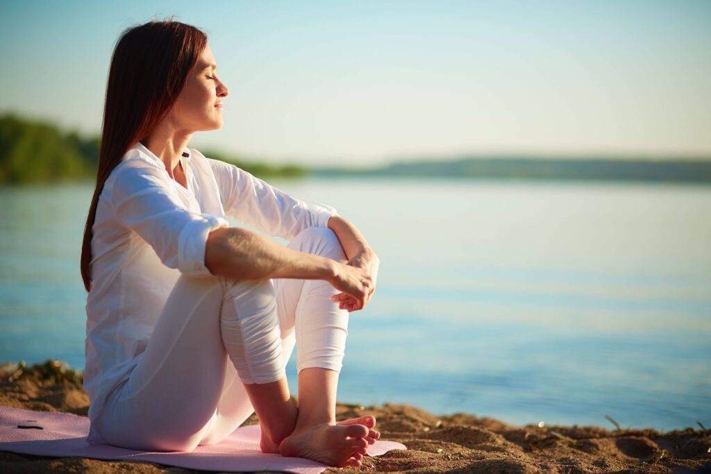 Femme assise au bord de l’eau, apaisée, représentant la détente et le lâcher-prise pendant un parcours PMA grâce à la sophrologie.