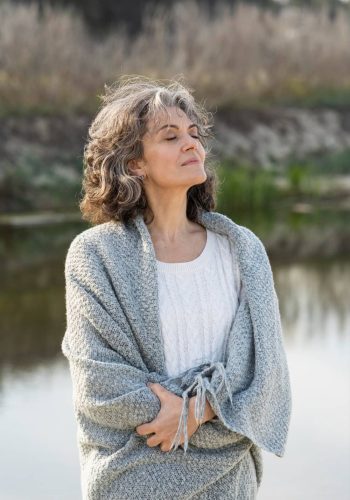 Femme aux cheveux grisonnants respirant face à un lac, symbole d’équilibre et de sérénité pendant la ménopause